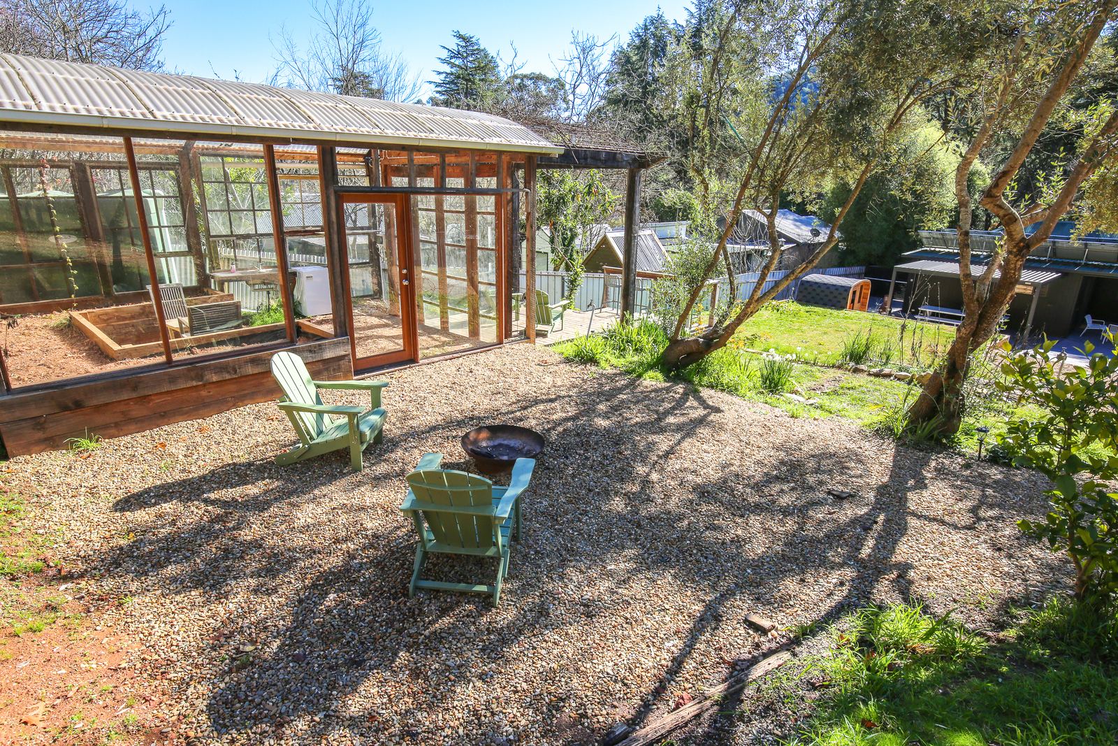 The fire pit on the gravel, with two chairs beside it and the glasshouse behind